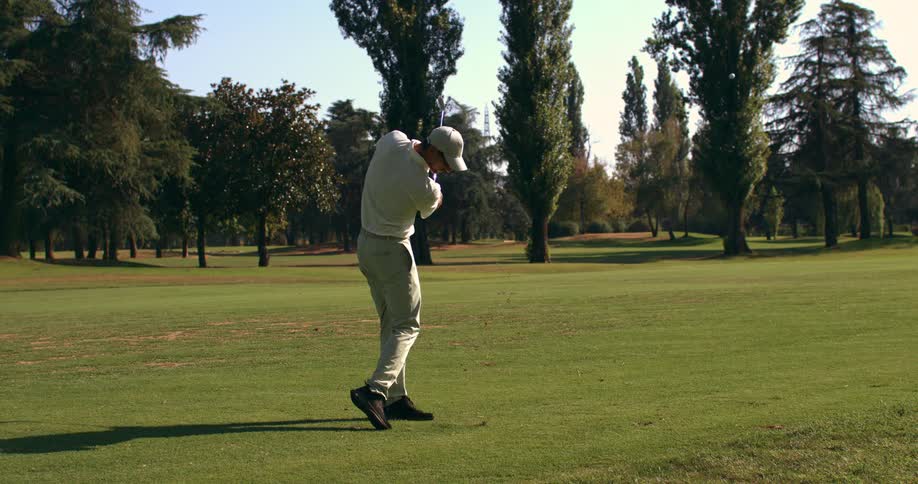 Slow motion shot of a man hitting a golf ball with an iron on a sunny day at the golf course