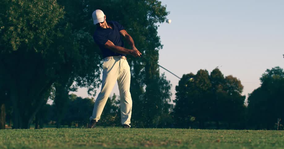 A male golfer executes a powerful drive off the tee in extreme slow motion on a beautiful golf course at sunrise
