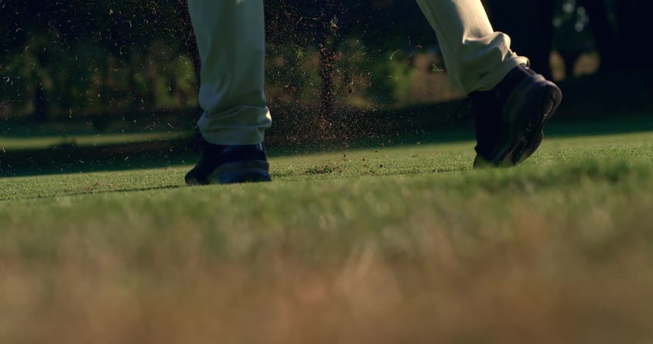 Slow motion closeup of a golfer hitting an iron shot, creating a divot as the ball launches from the green fairway