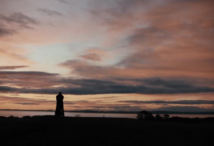 A silhouetted golfer takes a practice swing and then hits a ball on a coastal course as the sun sets