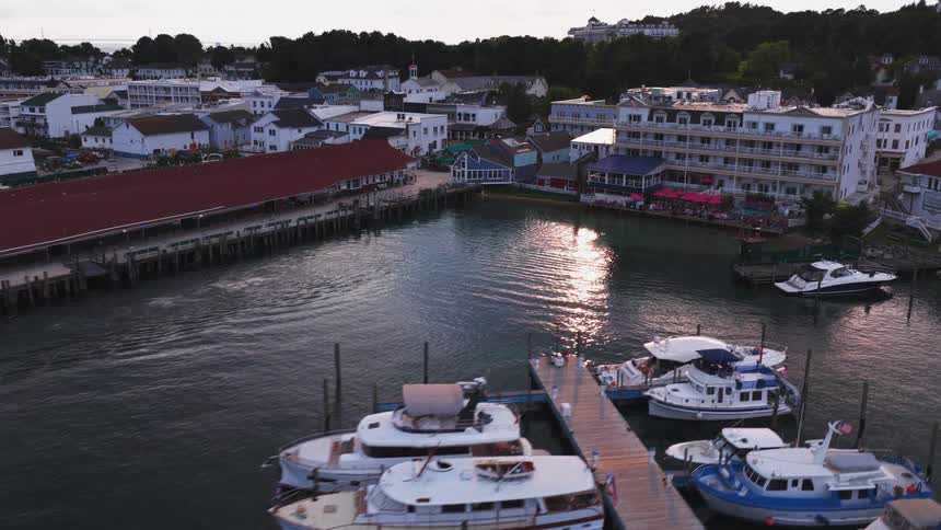 Aerial view of a ferry arriving at the Mackinac Island harbor at sunset, flying over the docks and into the charming downtown area