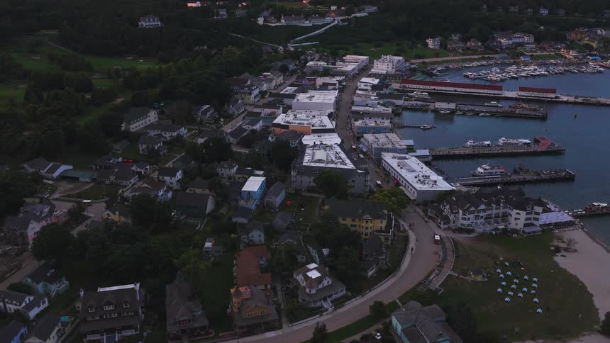 A serene aerial shot slowly reveals the quaint coastal town and harbor of Mackinac Island at dusk