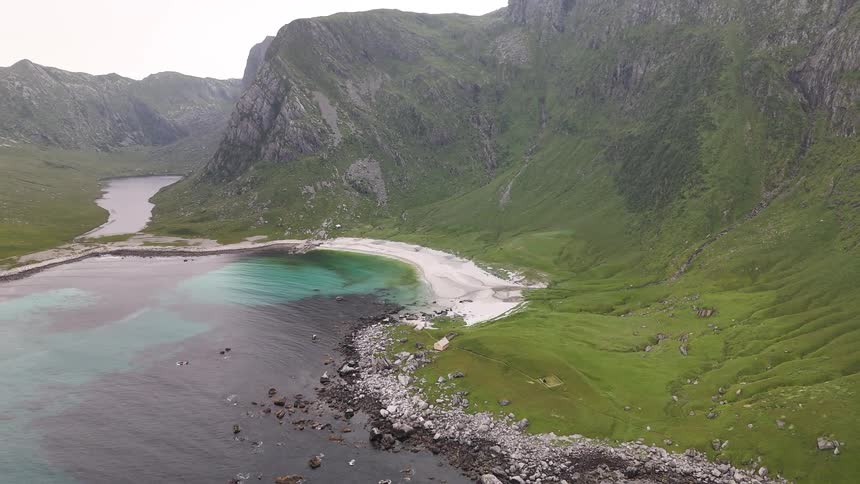 Static aerial view of a secluded white sand beach and turquoise cove nestled between towering green mountains