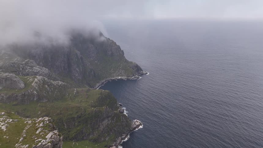 Fog slowly dissipates to reveal a majestic and rugged cliffside overlooking the vast ocean