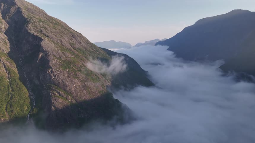 A static aerial shot captures a breathtaking Norwegian fjord blanketed in a thick layer of clouds