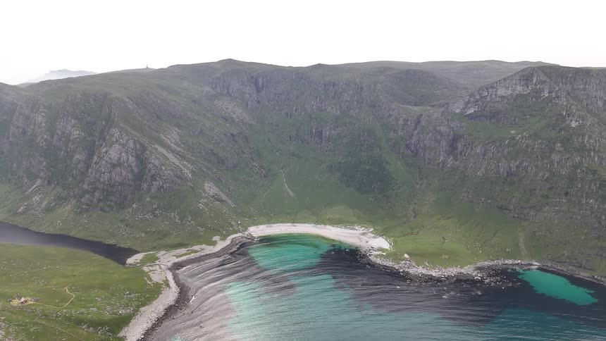 A serene, static aerial view showcases a pristine white sand beach and vibrant turquoise sea embraced by rugged green mountains
