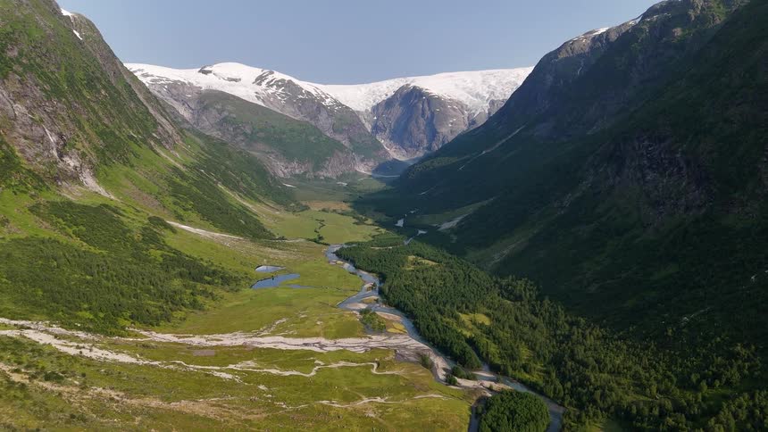 A majestic aerial view of a verdant valley with a winding river leading to a stunning glacier in the mountains of Norway on a sunny summer day