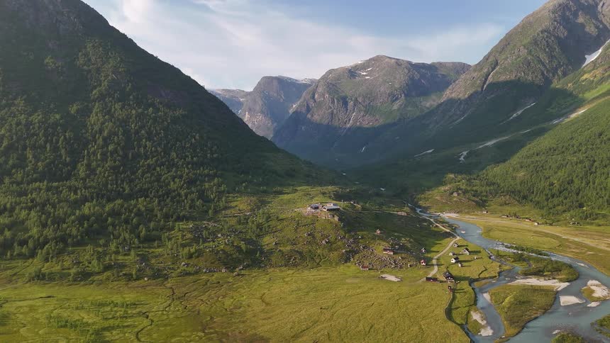 Static aerial shot of a picturesque Norwegian mountain valley with a small village and a clear blue river flowing through the green landscape