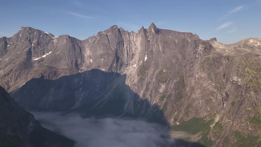 A static shot of the immense and rugged Troll Wall mountain in Norway standing tall above a tranquil sea of clouds filling the valley