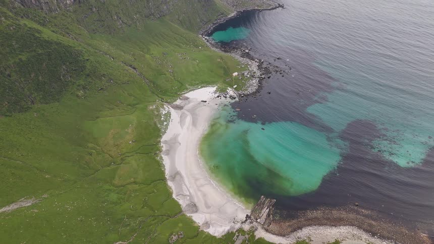 A majestic high aerial view reveals a stunning secluded white sand beach with crystal-clear turquoise waters at the base of a lush green mountain