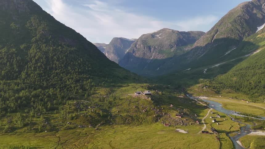 A static aerial view captures the majestic beauty of a remote mountain valley with a river winding through a small village