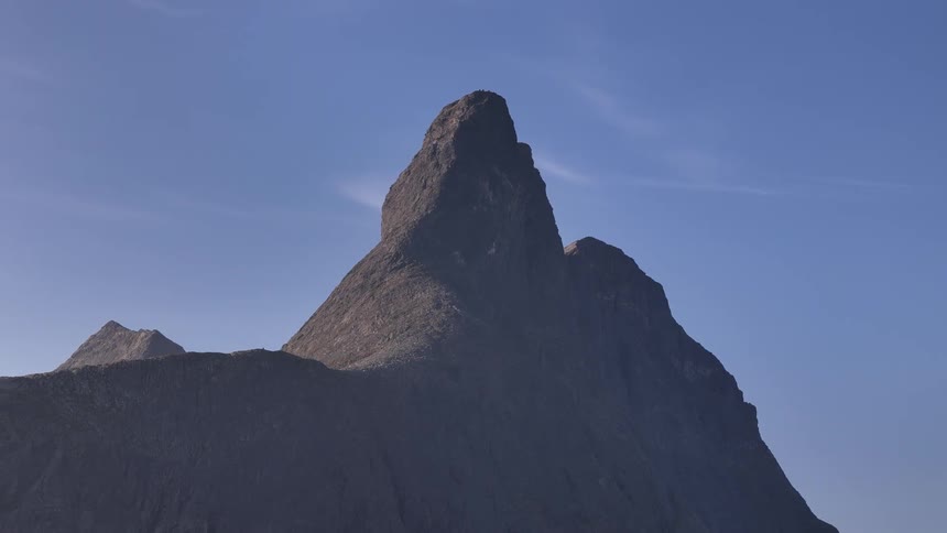 A majestic, rugged mountain peak stands tall against a clear, serene blue sky