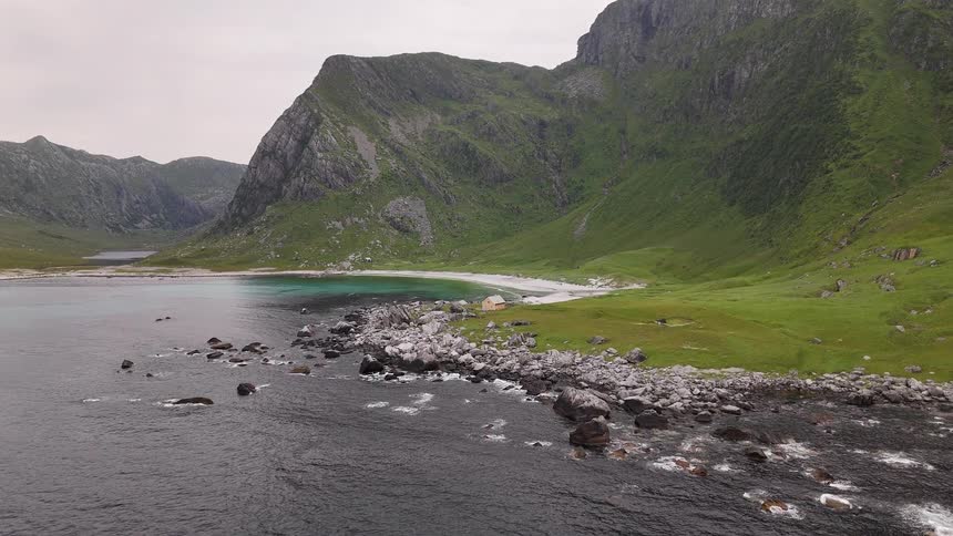 A majestic aerial view reveals a secluded turquoise bay nestled amongst towering green mountains on a rugged coastline