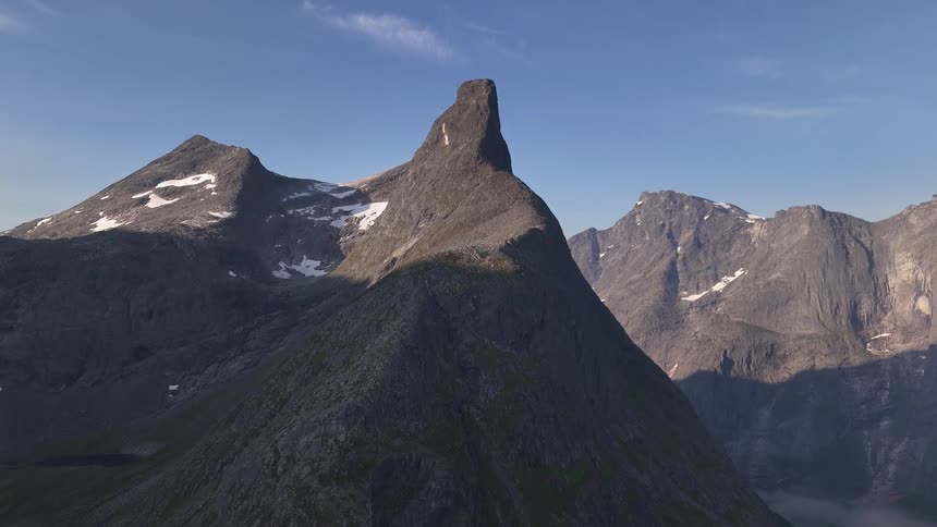 A majestic, uniquely shaped mountain peak is bathed in the golden morning sun amidst a rugged, shadowed mountain range