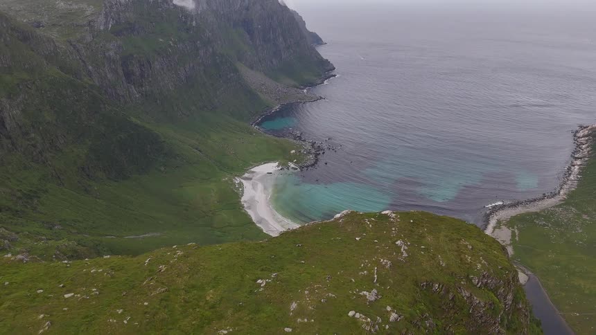 A dramatic aerial view showcases a stunning hidden beach with pristine turquoise waters nestled between towering green cliffs along the rugged coastline