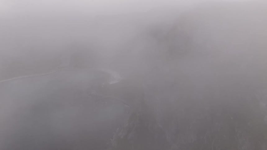 Aerial drone footage flying through thick fog to reveal a stunning hidden beach and turquoise bay surrounded by majestic green mountains