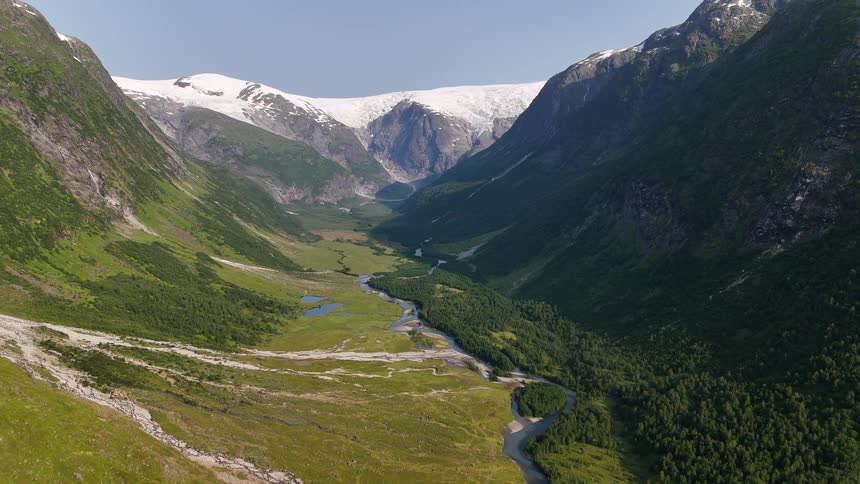 Spectacular aerial view of a vast green valley with a winding river, framed by steep mountains and capped by a large glacier under a clear blue sky