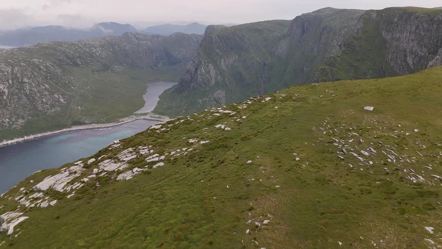 An aerial drone flies through thick clouds to reveal a stunning secluded cove with a white sand beach and turquoise water nestled between majestic mountains