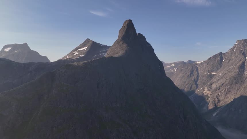 Majestic aerial pullback reveals a dramatic, sharp mountain peak in the stunning Norwegian wilderness at sunrise