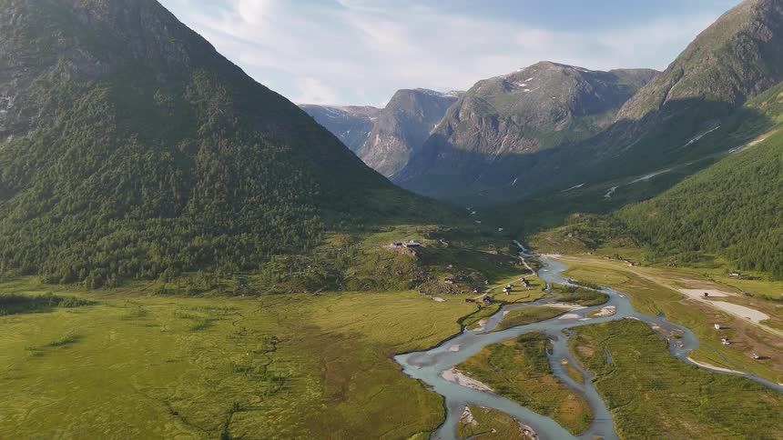 An epic aerial shot reveals a wide, lush valley with a winding glacial river nestled between towering mountains in Norway