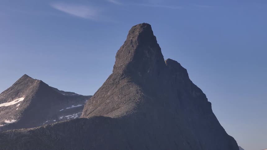 A static shot with a slow zoom out reveals the majestic scale of the Stetind mountain peak in Norway against a clear blue sky