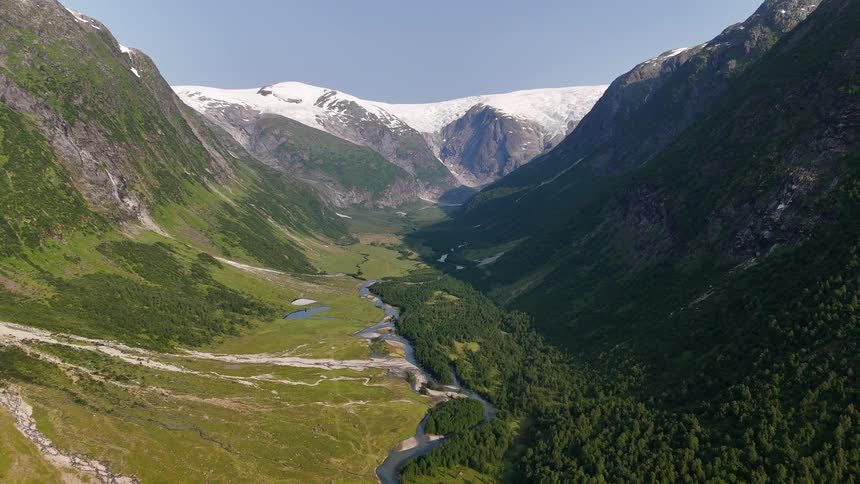 A breathtaking static aerial view of a wide, verdant mountain valley with a winding river leading to a distant glacier under a clear blue sky