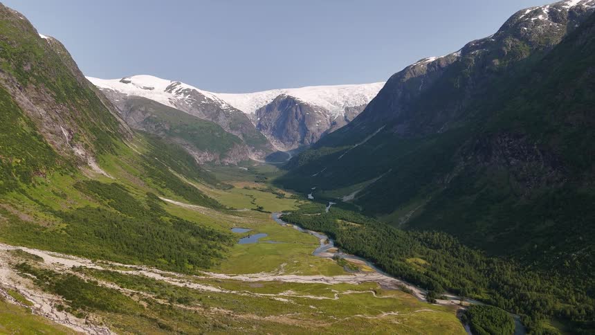 A majestic wide shot of the lush green Kjenndalen valley, with a meandering river leading to the stunning Kjenndalsbreen glacier in Norway
