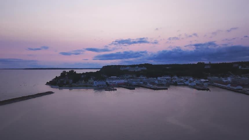 A stunning aerial view captures the serene harbor of Mackinac Island at twilight, with calm waters reflecting the pastel-colored sky