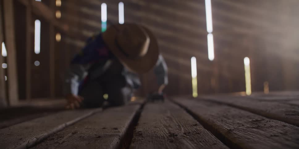 A little boy wearing a cowboy hat plays with his toy truck on the rustic wooden floor of a barn