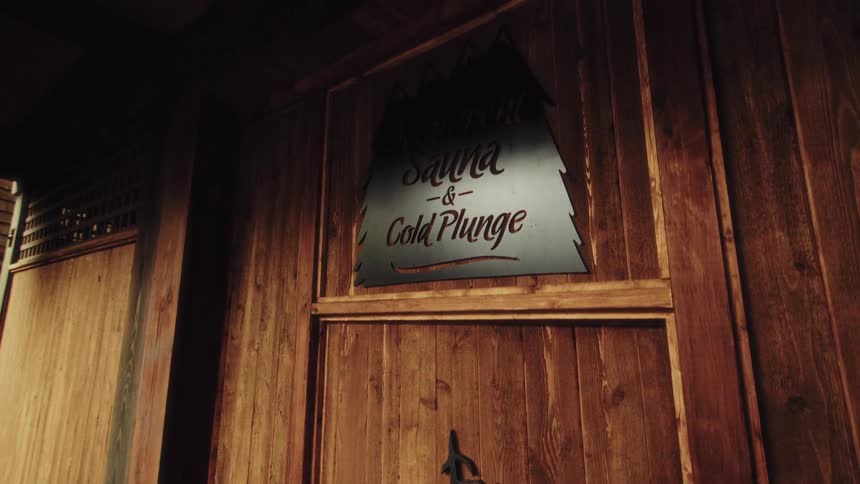 A decorative sign for an oceanfront sauna and cold plunge hangs on a rustic wooden wall