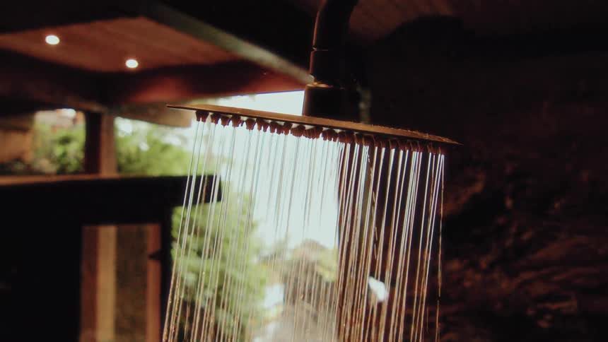 A rainfall shower head turns on, releasing a gentle stream of water in a luxurious, rustic bathroom