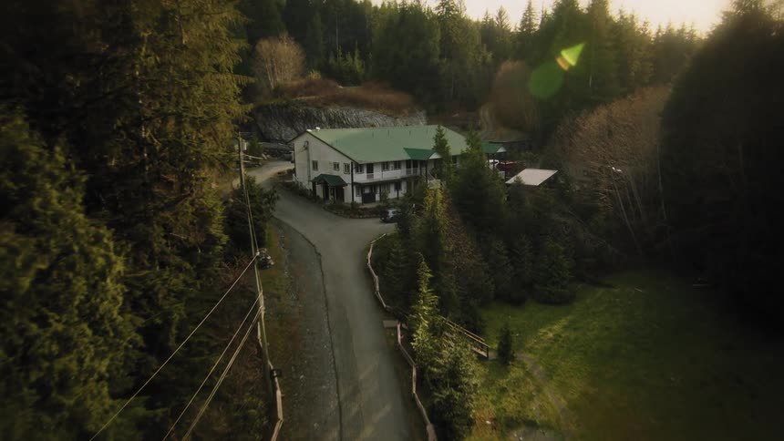 A slow aerial approach towards a secluded mountain lodge surrounded by a vast evergreen forest at golden hour