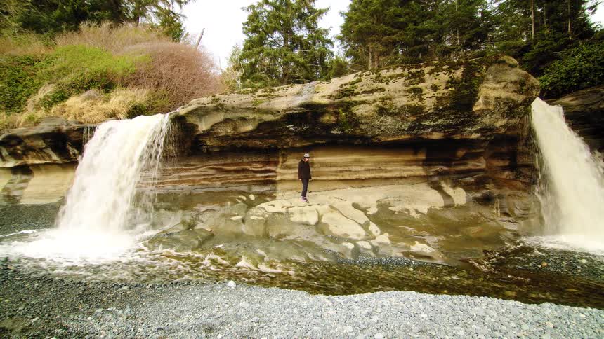 A person explores a stunning natural wonder, walking on a rocky ledge between two powerful waterfalls