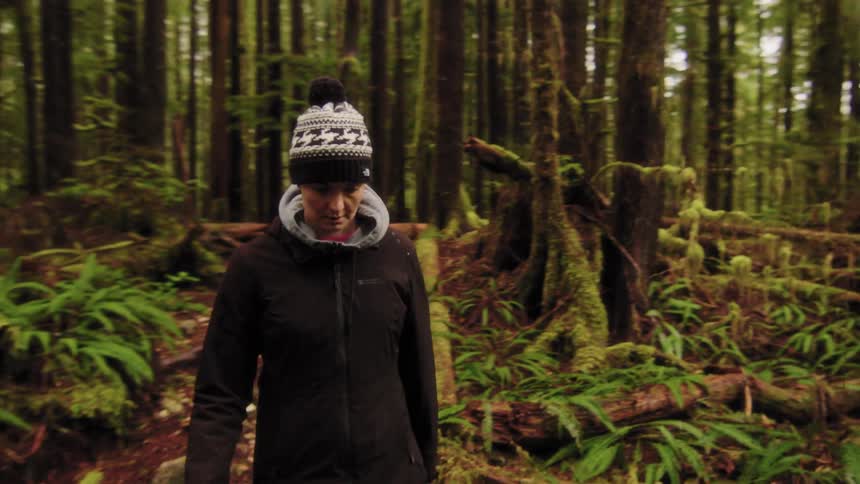 Slow motion tracking shot of a woman in a beanie hiking through a beautiful, moss-covered temperate rainforest