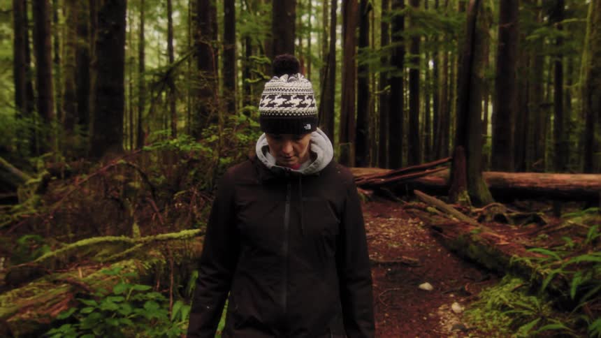 A woman in a winter hat hikes along a path through a lush, mosscovered Pacific Northwest rainforest