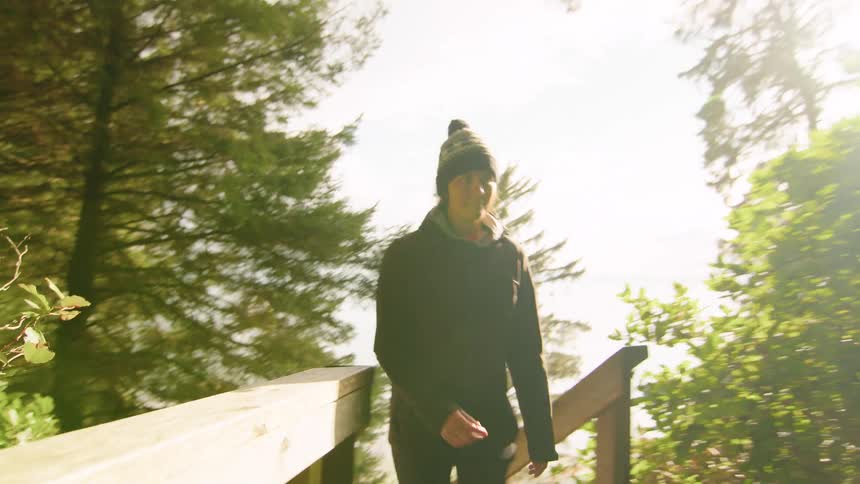 Slow motion shot of a hiker in a beanie walking up a wooden staircase on a forest trail with sunlight filtering through the trees