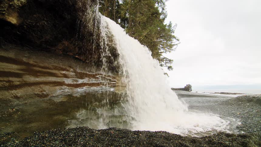A serene cinemagraph loop shows a waterfall cascading from a forested cliff onto a rocky shoreline