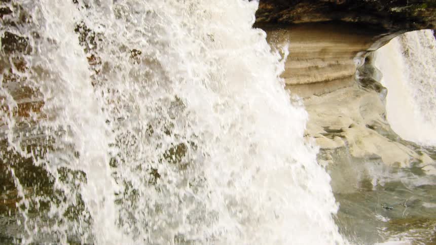 A powerful forest waterfall tumbles over a rocky ledge in a dramatic slow-motion close-up