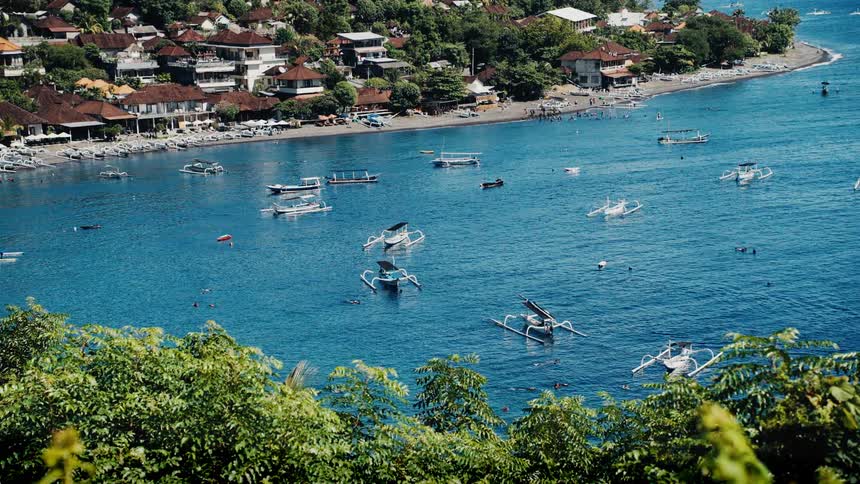 A scenic high-angle view of a tropical bay in Bali with traditional jukung boats floating on the clear blue water
