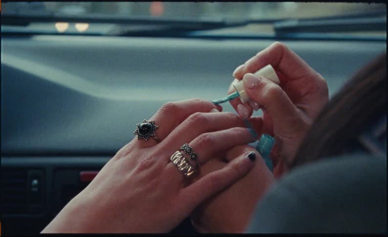 Vintage-style footage shows a close-up of a girl painting her friend's nails with turquoise nail polish in a car