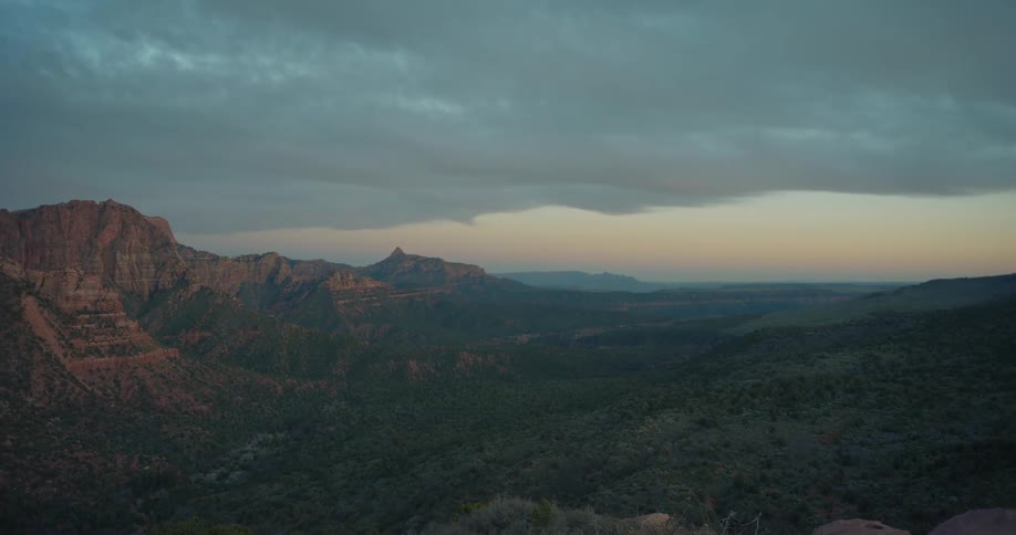 A camera tilts up from a rocky cliff edge to reveal a breathtaking view of a mountain valley at dusk