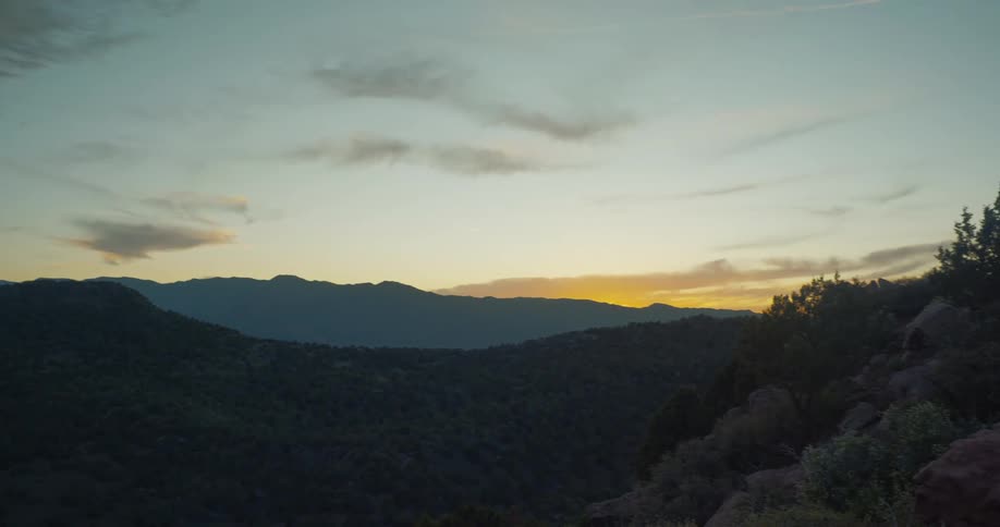 A tranquil sunset casts a warm, golden glow over a vast, forested mountain range