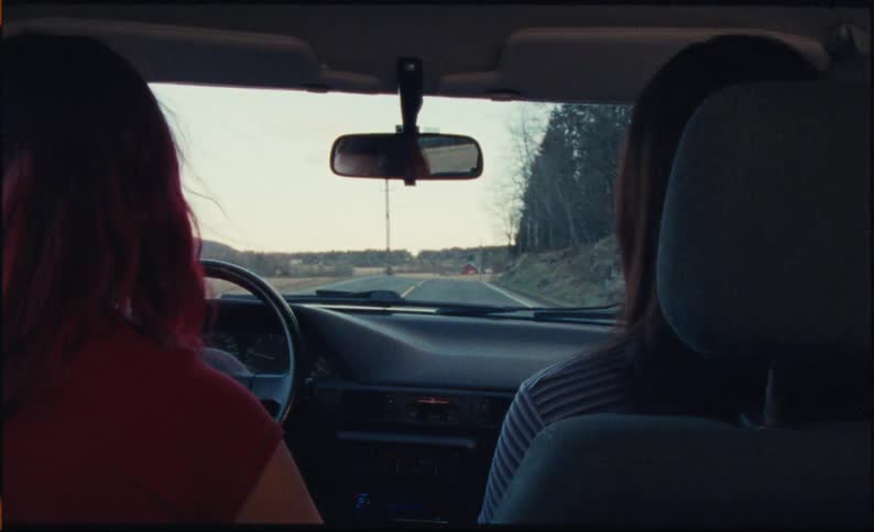 Two young women friends enjoy a scenic drive down a country road, seen from the backseat perspective