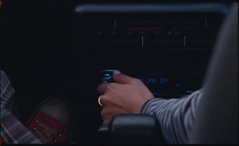 A close-up of a person's hand adjusting the volume and changing the station on a car radio in a dark vehicle