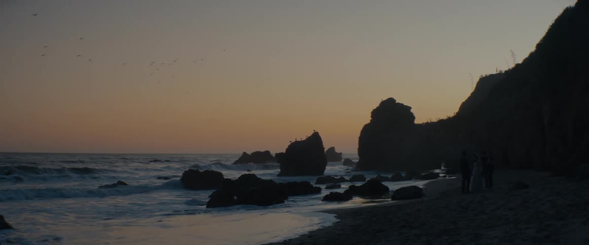 A serene view of a rocky coastline at dusk with gentle waves and birds flying in the sky