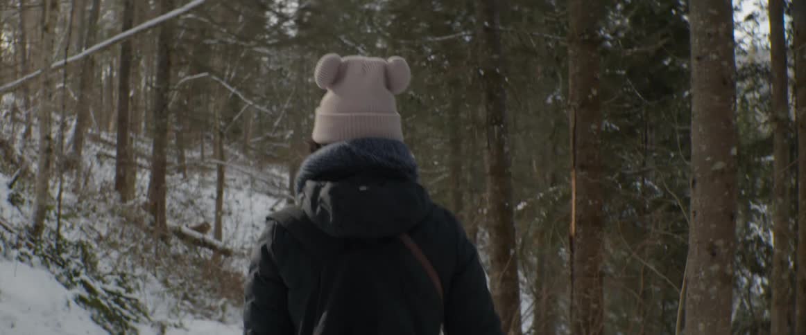 A woman wearing a cute pom-pom beanie walks through a snowy forest on a cold winter day