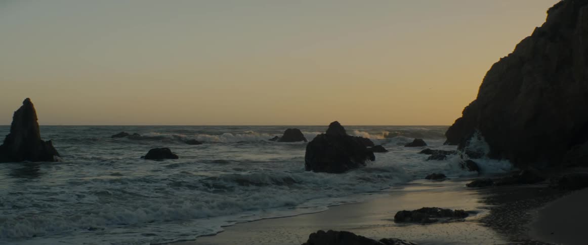 Ocean waves crash in slow motion against a rocky shoreline during a golden sunset
