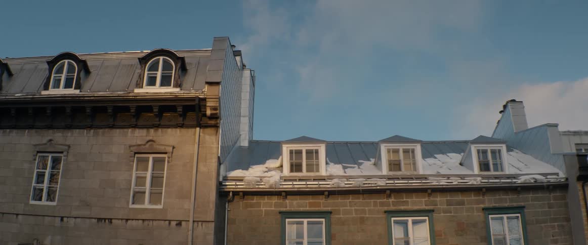 Snow-covered rooftops of historic stone buildings against a clear blue winter sky at sunset