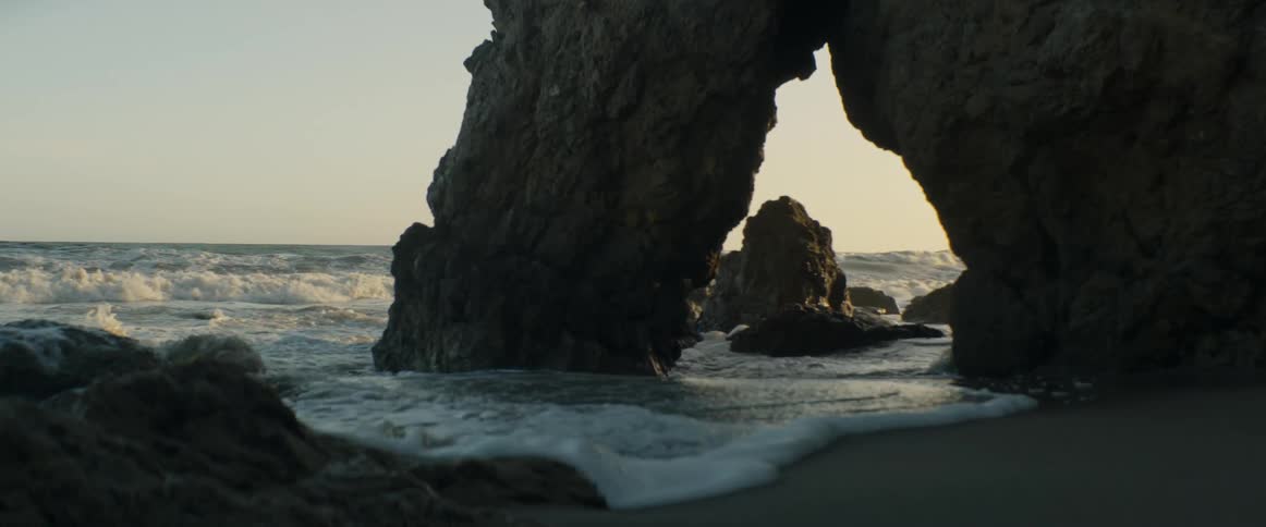 Slow motion waves gently wash ashore around a stunning rock arch on the beach at sunset