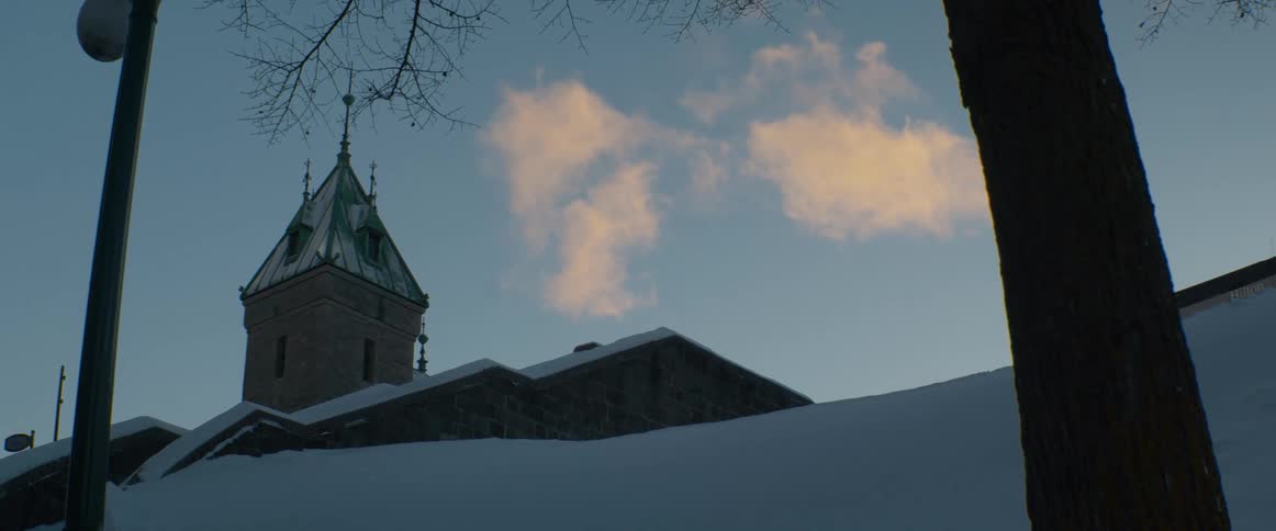 Golden clouds float above a snow-covered stone building with a tower during a winter sunset